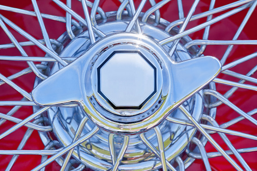 Close up of a mid 20th century English classic sports car, wire spoked wheel with a sparkling chrome finish. Copy space.