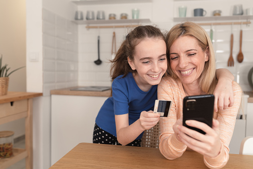 Mother sitting with her little daughter while making an online payment at home