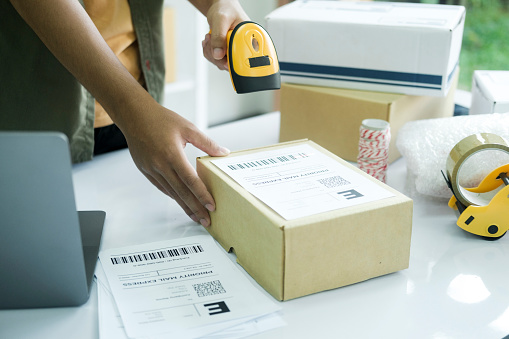 Young male online store seller, owner holding scanner scanning parcel barcode before delivery or shipping to customer. an working at factory warehouse scanning labels on the boxes. E-commerce concept.