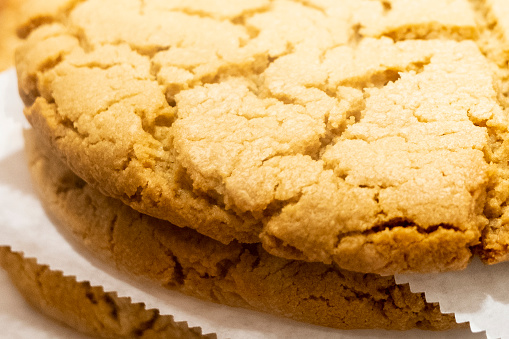 A close up macro photograph of an oversized peanut butter cookie stacked on top of a baking sheet on top of more cookies.