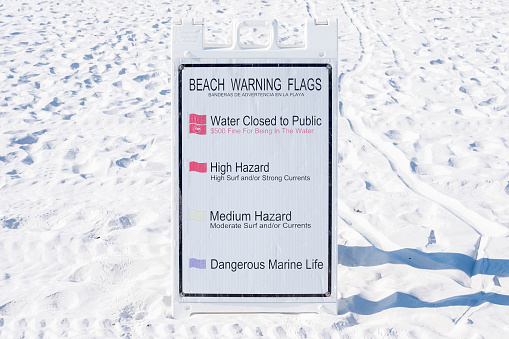 A warning flags sign on a white sand beach.