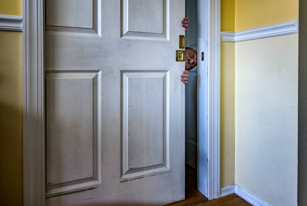 Young adult man wearing traditional Catrina makeup peeking through a doorway while holding a candle during Day of the Dead / Halloween celebrations in Mexico