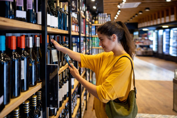 woman shopping at a liquor store and scanning a label on a bottle of wine - healthy eating food and drink nutrition label food imagens e fotografias de stock