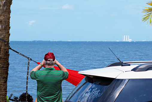 Titusville, Florida, USA - May 30, 2020: A man looks through binoculars toward the Kennedy Space Center launch complex during the Space-X Crew Dragon Demo-2 launch carrying NASA astronauts Douglas Hurley and Robert Behnken to the International Space Station with NASA’s massive Vehicle Assembly Building (VAB) visible in the distance.