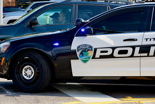Titusville, Florida, USA - May 30, 2020: A couple waits in their vehicle as a City of Titusville police car blocks their access at an accident scene.