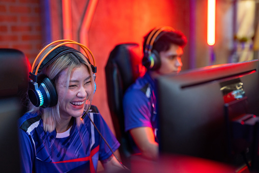 Asian gamers expressing success while raising hands up and smiling during participation in esports tournament.