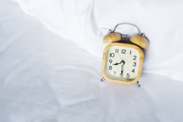 istock Wood alarm clock at 8 on white bed background 1438540588