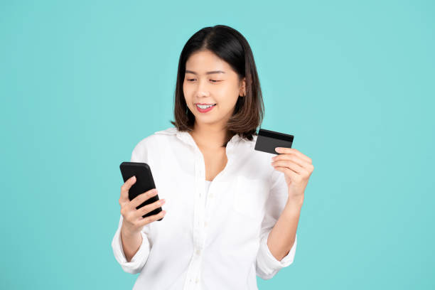 istock Happy young asian woman standing isolated on bright green background. She using mobile cell phone and hold credit bank card. People lifestyle concept. Mock up copy space. 1438542814