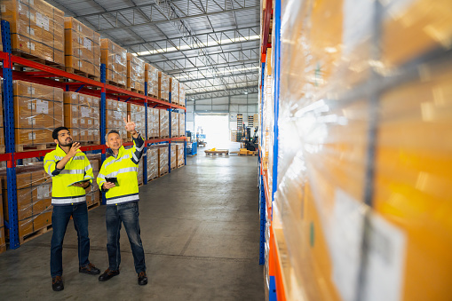 Workers checking goods stock on shelf in warehouse inventory using digital tablet.