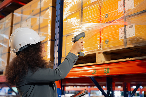 Asian Woman worker working uses a barcode reader to scan a product inside boxes on a shelf rack to receive into an inventory system.