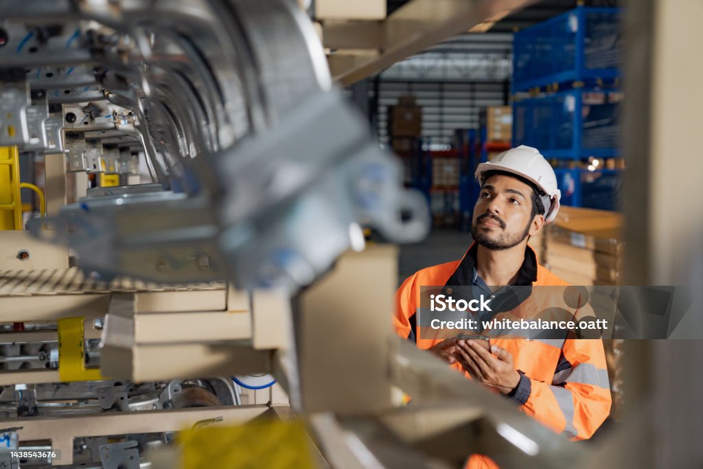 A day at work for a male and female engineers working in a metal manufacturing industry. Young man industrial engineer wearing a white helmet while check the welding on the production line in the factory. Manufacturing Stock Photo