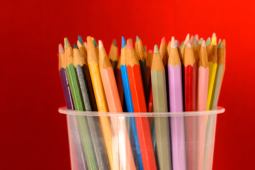 Color pencils in pencil tray on red background.