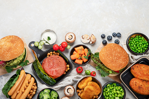 Plant-based food concept-vegan burgers, sausages, vegetarian nuggets, fresh vegetables and sauces on a white background. Top view.