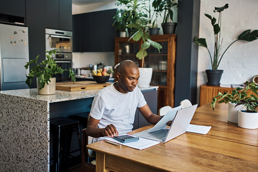 Budget, accounting and businessman in his home with laptop and paperwork for financial planning, document or profit review. Black man entrepreneurship or home finance analysis of bills or bank loan