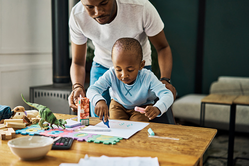 Black family, father and child drawing or learning writing in a coloring book for educational development at home. Love, artistic and African daddy helping or teaching his creative son, kid or boy