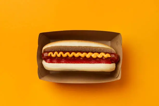 Photo of Classic hot dog with wurst, ketchup and mustard on orange background. Restaurant menu delivery tacke away concept