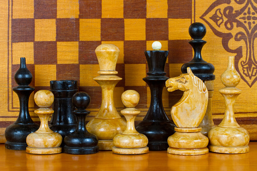 Old chess pieces on the background of a wooden chessboard. Handmade wooden chess.