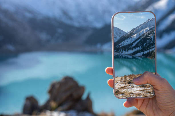 istock Hand with a phone taking image of a turquoise lake surrounded by mountains 1438561266