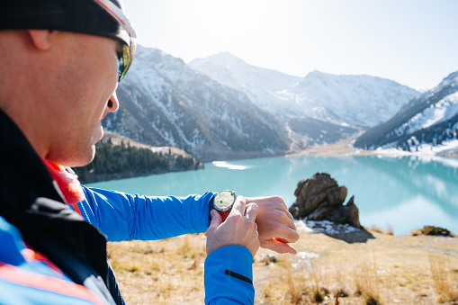 Man checking a map on his smartwatch with points of interest marked. Blurred beautiful mountain lake in background. On a sunny day.