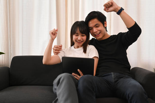 istock Overjoyed young Asian couple looking at digital tablet, celebrating achieve or getting good surprising news. 1438561375