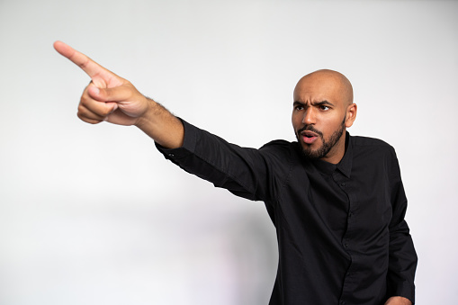 Portrait of impressed young man pointing finger at ad. Shocked multiethnic male model with bald head and beard in black shirt looking away, showing ads with open mouth. Shock, advertisement concept