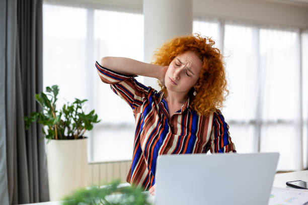 istock Feeling exhausted. Frustrated young woman looking exhausted and massaging her neck while sitting at her working place 1438562165