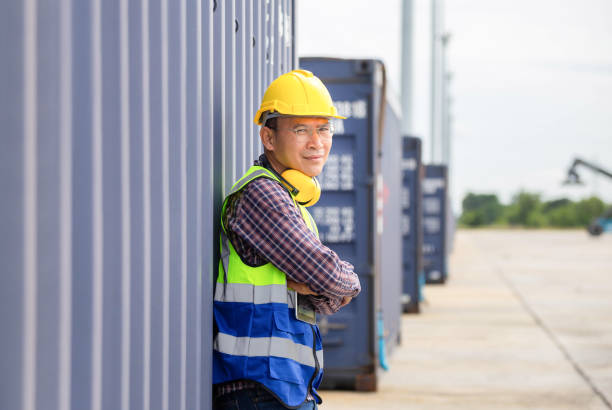 istock Relaxing engineer man in industry containers cargo, Foreman dock worker in hardhat and safety vest control loading containers box from cargo 1438563544