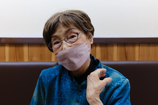 A senior woman with a face mask sitting.