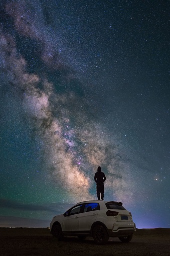 A man in a car the lights on and nebulas and galaxies in the dark starry sky
