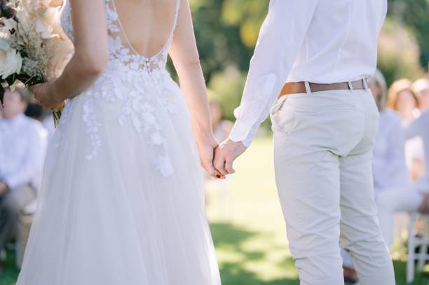 istock Bride and groom both dressed in white holding hands at their wedding and saying their vows 1438574648