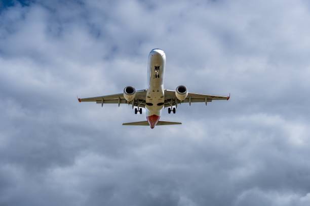 istock Low angle of a white passenger airplane in mid-air with a cloudy background during daytime 1438576464