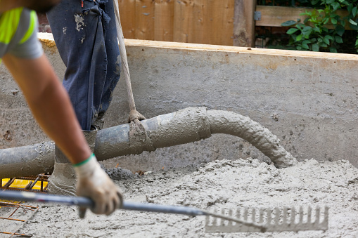 Pouring of industrial concrete into wooden shuttering and rebar to create a building foundation slab, being levelled by a construction worker