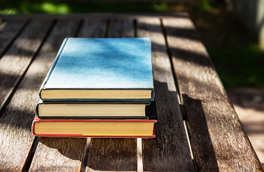 A wooden table with three books on top of each other at daytime