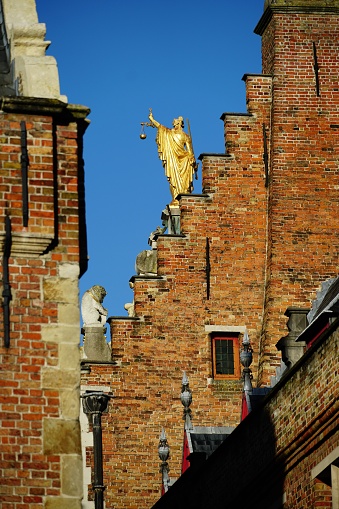 A vertical backside view of the golden Justitia statue on top of the old courthouse in Bruges, Belgium