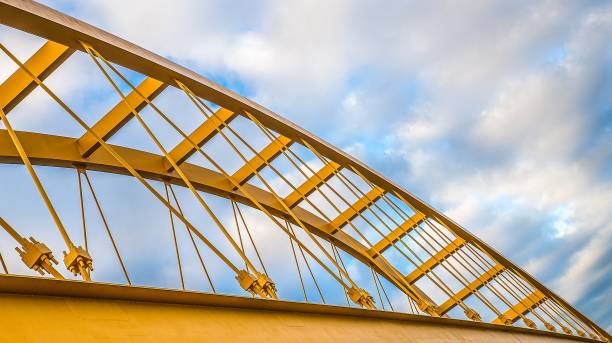istock Low angle shot of a yellow cable-stayed bridge with a blue cloudy sky in the background 1438581801