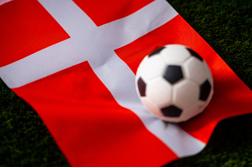 Denmark national football team. National Flag on green grass and soccer ball. Football wallpaper for Championship and Tournament in 2022. World international match.