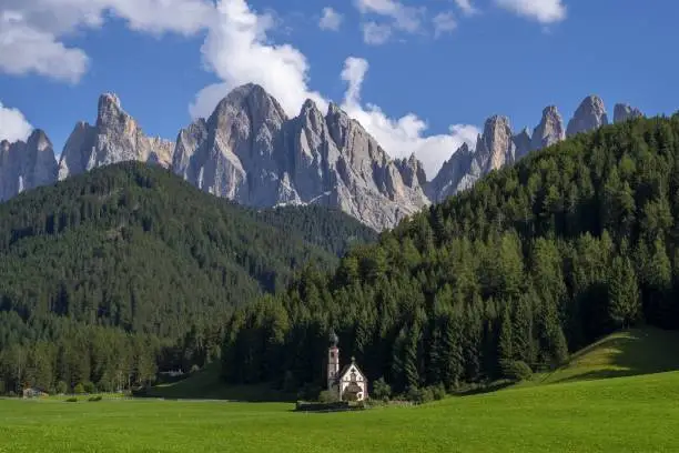 A church in a green landscape surrounded by rocky mountains in Funes Valley,  St. Italy