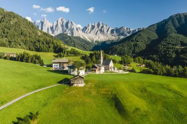 Photo of High angle shot of a lot of buildings surrounded by high rocky mountains in Funes Valley, St. Italy