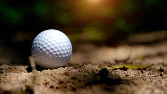 Golf ball on the sand in beautiful golf course at sunset background.  Golf ball close up in golf coures at Thailand