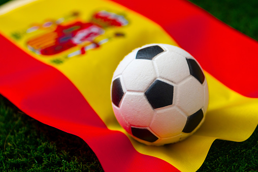 Spain national football team. National Flag on green grass and soccer ball. Football wallpaper for Championship and Tournament in 2022. World international match.