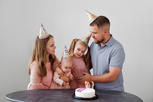 Caucasian family celebrates child birthday. Mom, dad and two baby daughters with cake and candles isolated on white background