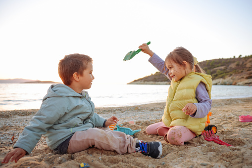 Happy little girl and boy building sandcastle on the beach