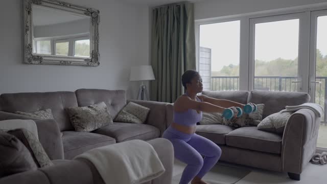 Woman doing squats with dumbbells at home