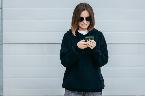 Young woman in glasses and black hoodie with smartphone in hand