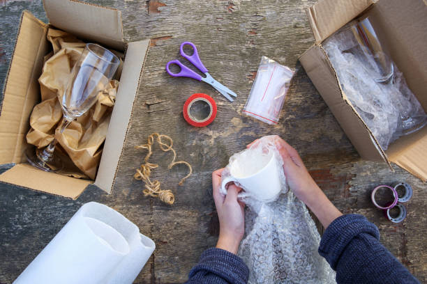 A woman packs a glass cup in a plastic bubble pack. Fragile package.