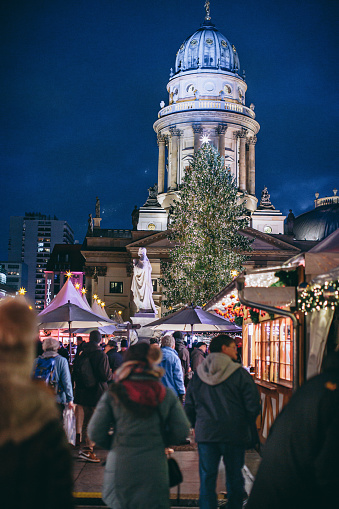 Gendarmenmarkt, traditional Christmas market on the square in front of illuminated German church with people visiting stalls in the evening