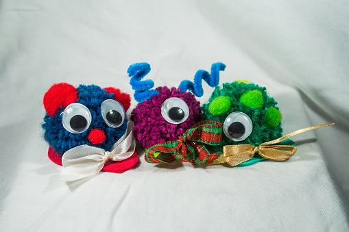 a close up shot of three woolly colorful toys with googly eyes and ribbons on a white cloth