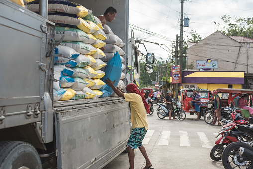 Sagbayan, Bohol, Philippines - May 2022: A porter unloads sacks of rice from a truck to the local market.