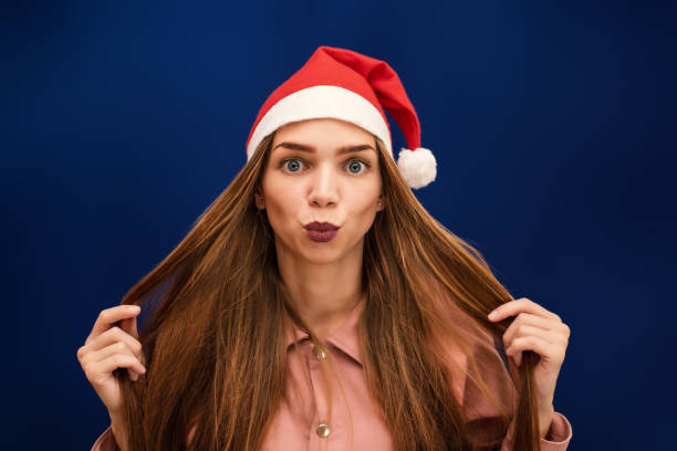 A girl in a Santa Claus hat on an isolated blue background sends a kiss stock photo