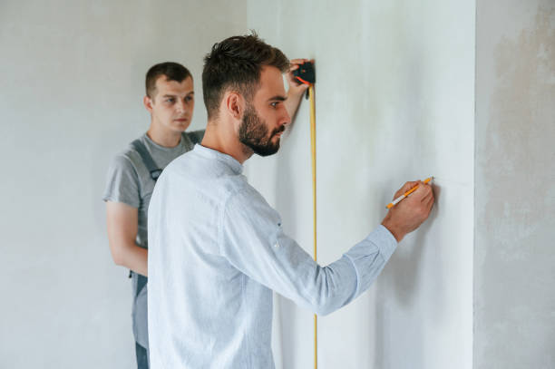 istock Measuring the wall by roller. Two men is making repairs in the apartment together 1438602945